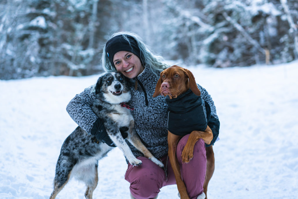 Blonde woman in the snow with her mini aussie and vizsla