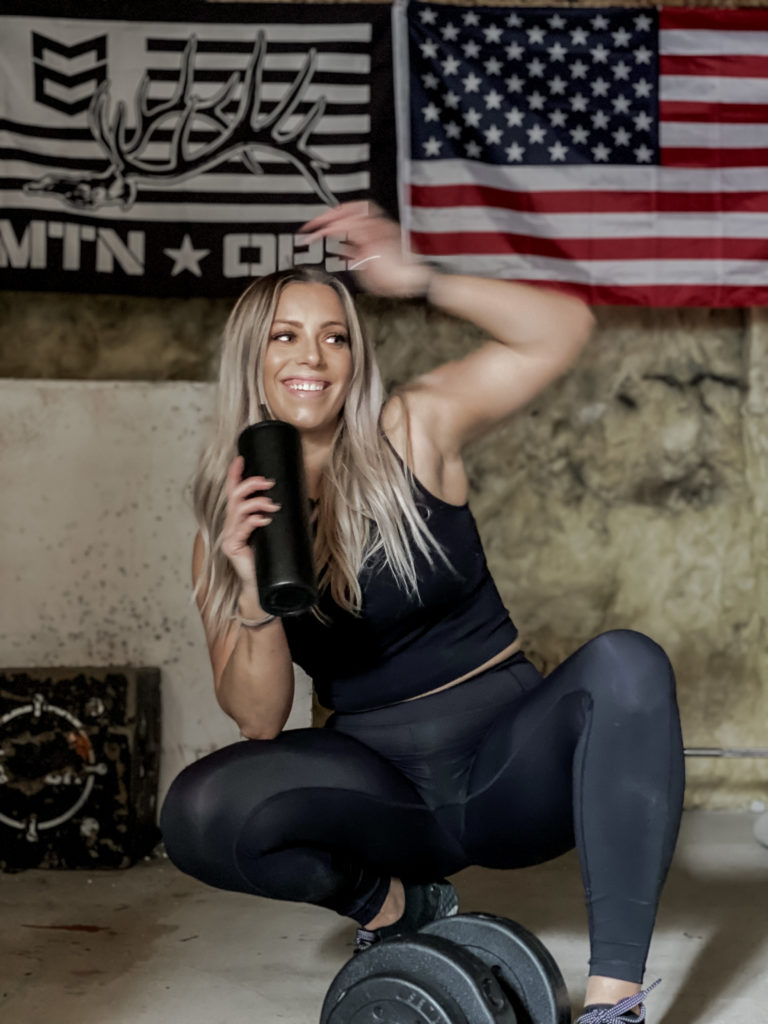 Brittney Long working out in all black, laughing while having a water break with the American Flag in the back